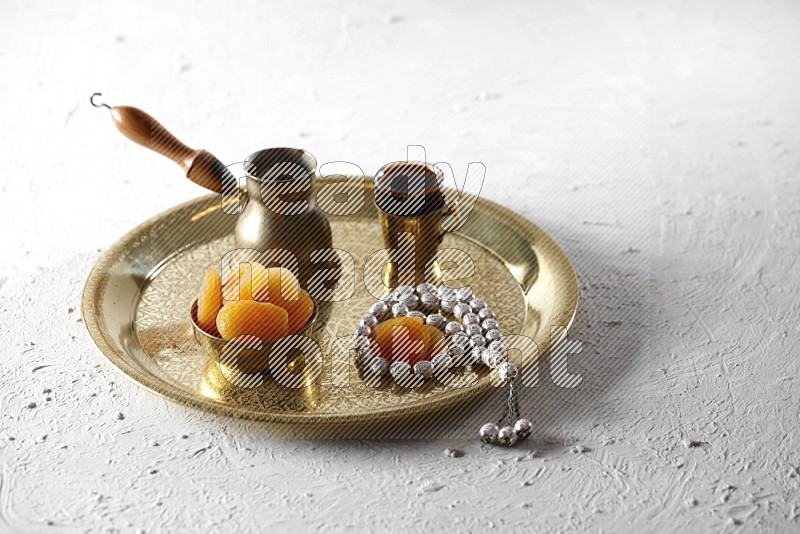 Dried apricots in a metal bowl with coffee and prayer beads on a tray in a light setup