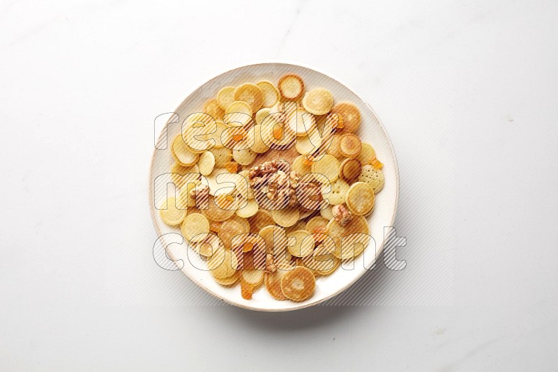 Top-view shot of walnut and apricot cereal pancakes in a round bowl on white background