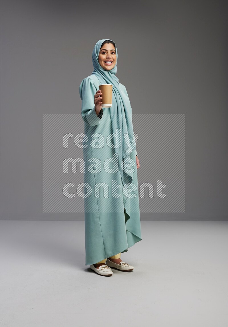 Saudi Woman wearing Abaya standing  holding paper cup on Gray background