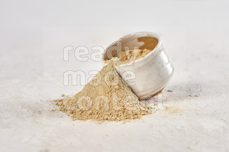 A beige pottery bowl full of ground ginger powder with fallen powder from it on white background