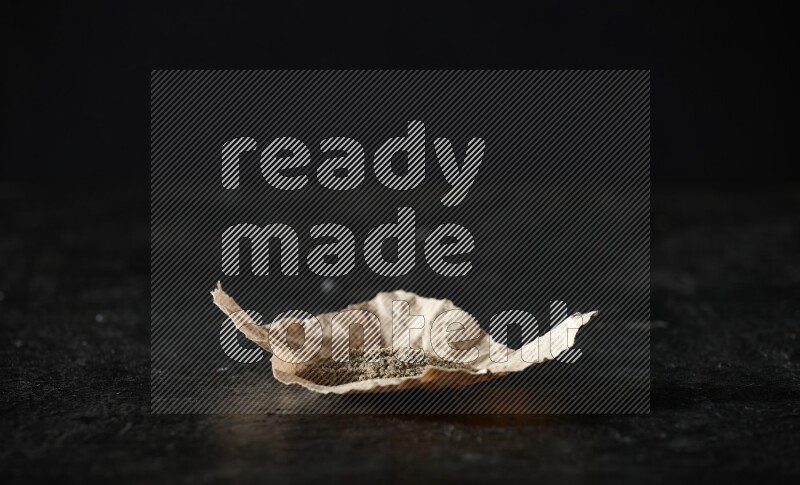 Cardamom powder in a crumpled piece of paper on textured black flooring