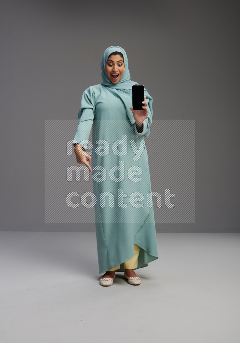 Saudi Woman wearing Abaya standing showing phone to camera on Gray background