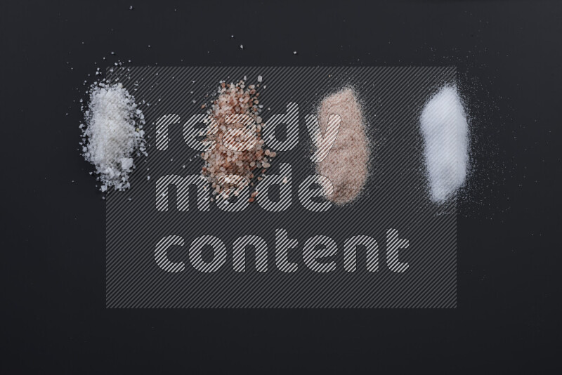 Bunches of table salt, coarse sea salt, fine himalayan salt and coarse himalayan salt on black background