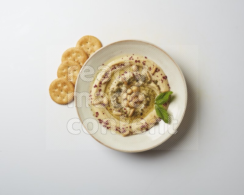 Hummus in a pottry plate garnished with zaatr & sumak on a white background