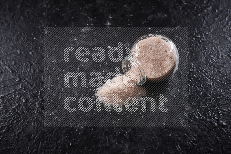 A glass jar full of fine himalayan salt on black background