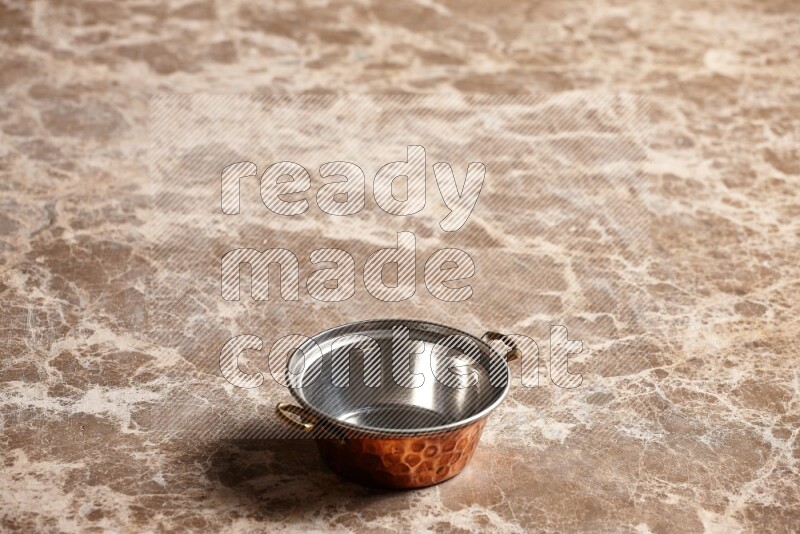A small copper pot on beige marble background