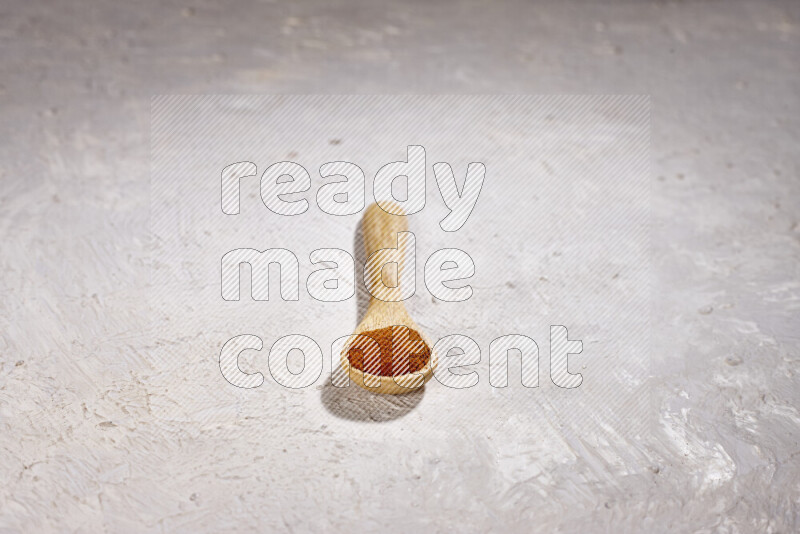 A wooden spoon full of ground paprika powder on white background