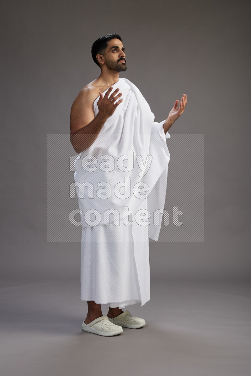 A man wearing Ehram Standing performing dua'a on gray background