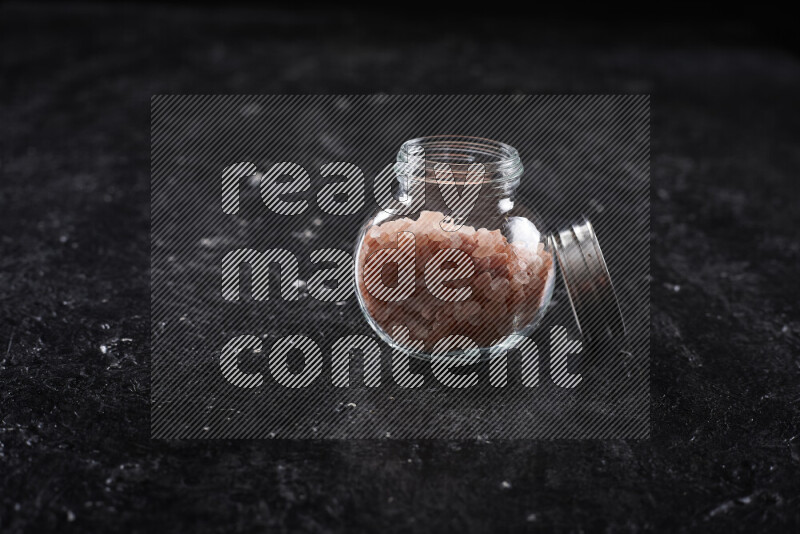 A glass jar full of coarse himalayan salt crystals on black background