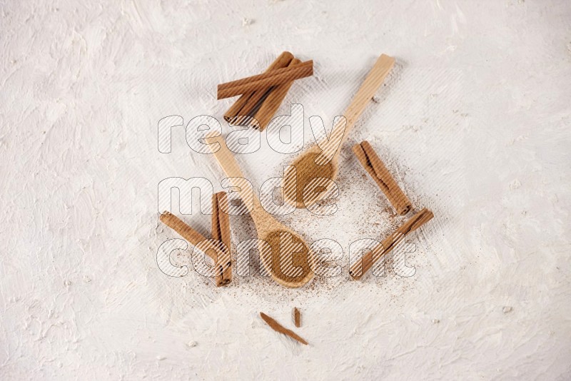 Two wooden spoons full of cinnamon powder with cinnamon sticks on white background