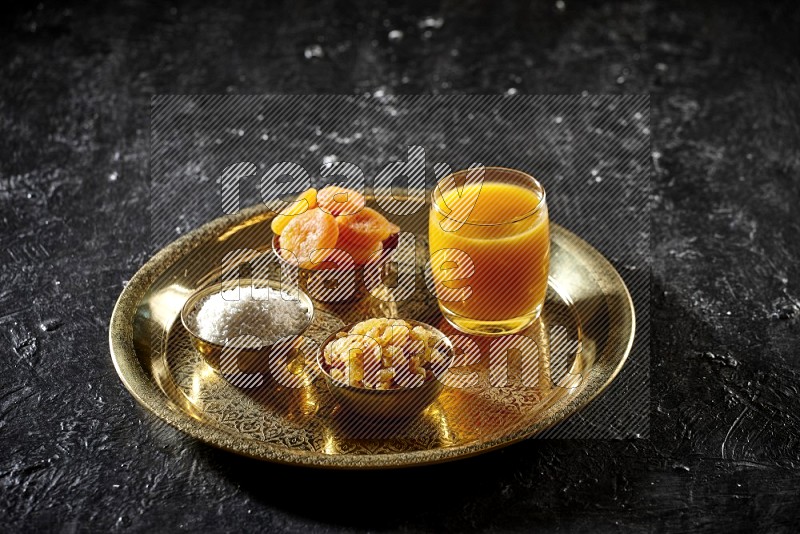 Dried fruits in metal bowls with qamar eldin on a tray in dark setup