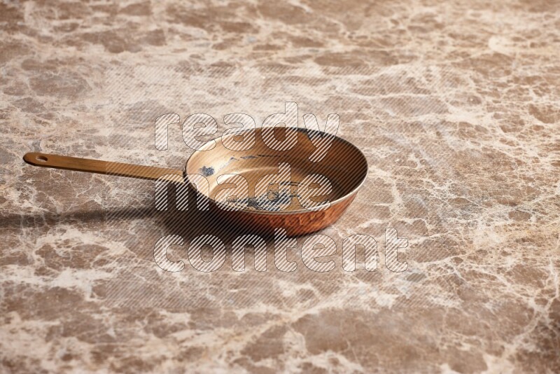 A small copper pan on beige marble background