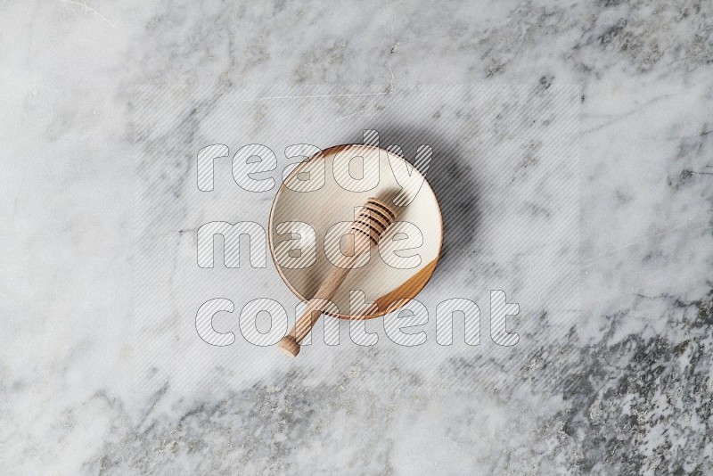 Multicolored Pottery Plate with wooden honey handle in it, on grey marble flooring, Top View