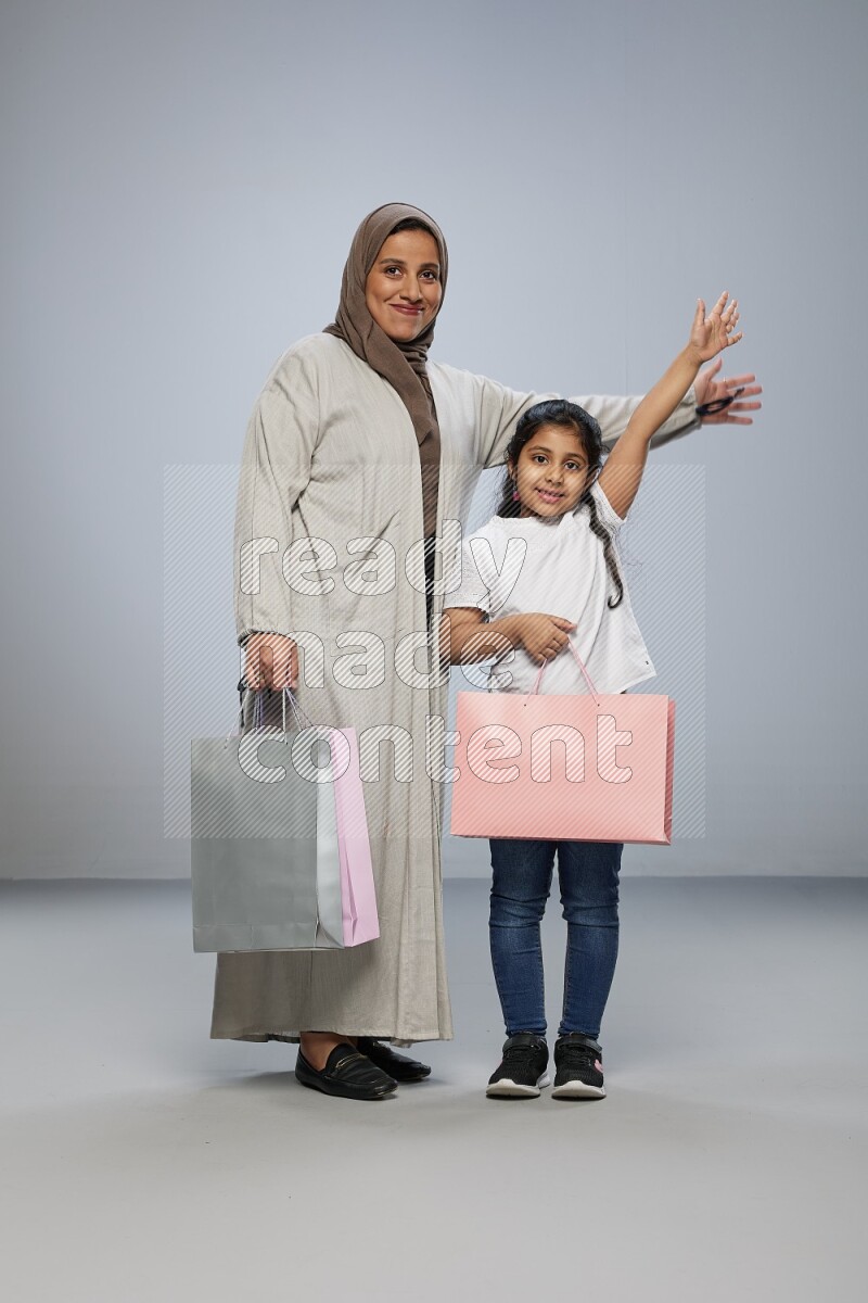 Mom and daughter holding shopping bags on gray background