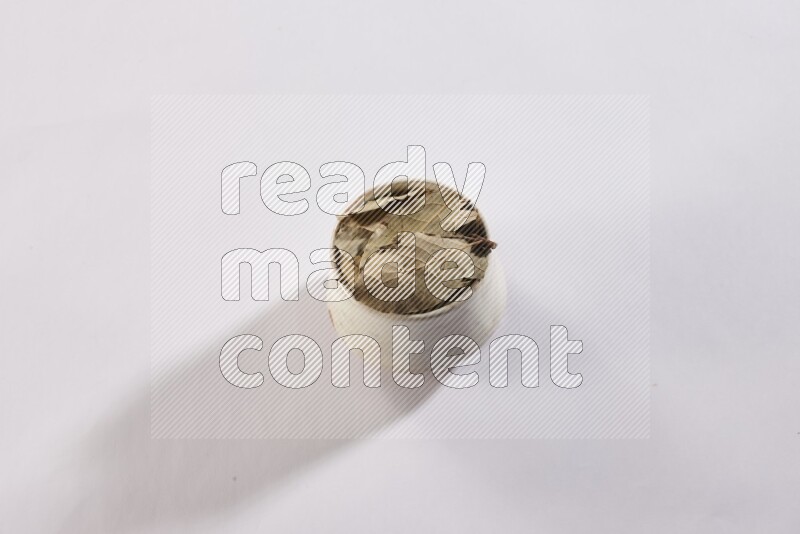 A beige pottery bowl full of dried bay leaves on white flooring
