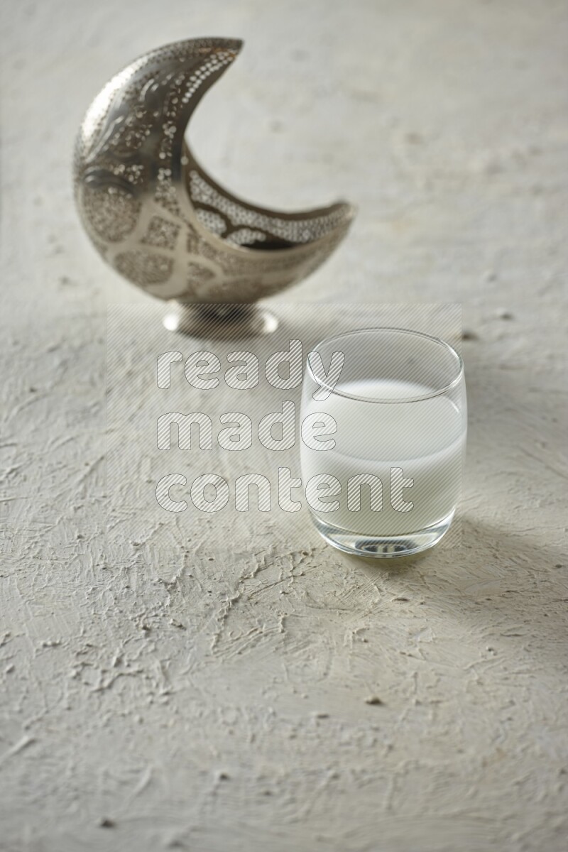 A silver lantern with different drinks, dates, nuts, prayer beads and quran on textured white background