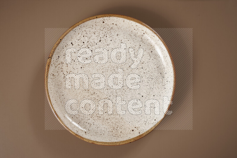 An assorted whole spices on a flat beige plate including fresh and dried ginger, cinnamon sticks, cardamom, turmeric fingers, cloves, star anise on a beige background