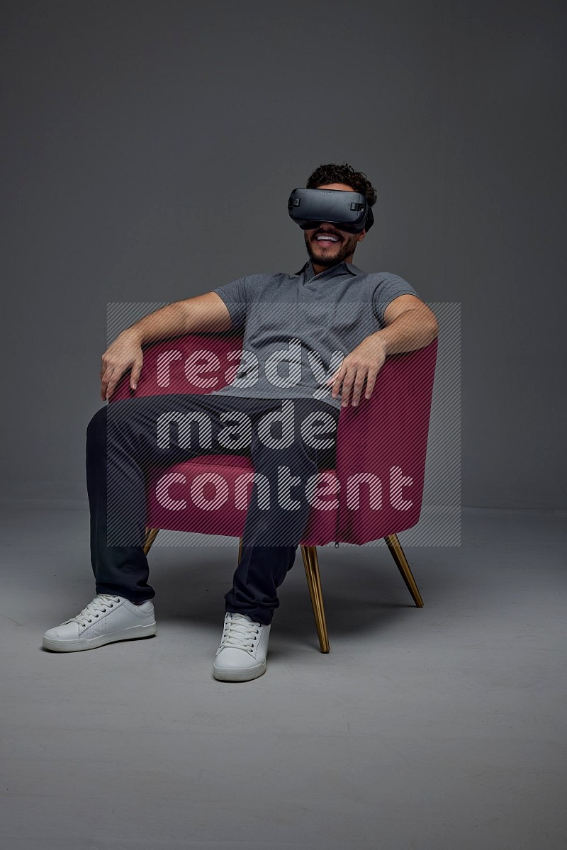 A man wearing casual and wearing VR while sitting on a burgundy chair eye level on a gray background