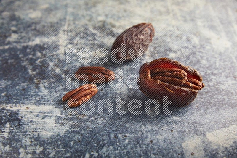 two pecan stuffed madjoul dates on a rustic blue background