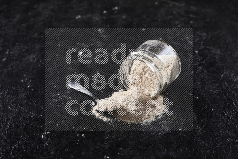 A glass jar full of onion powder flipped with some spilling powder on black background