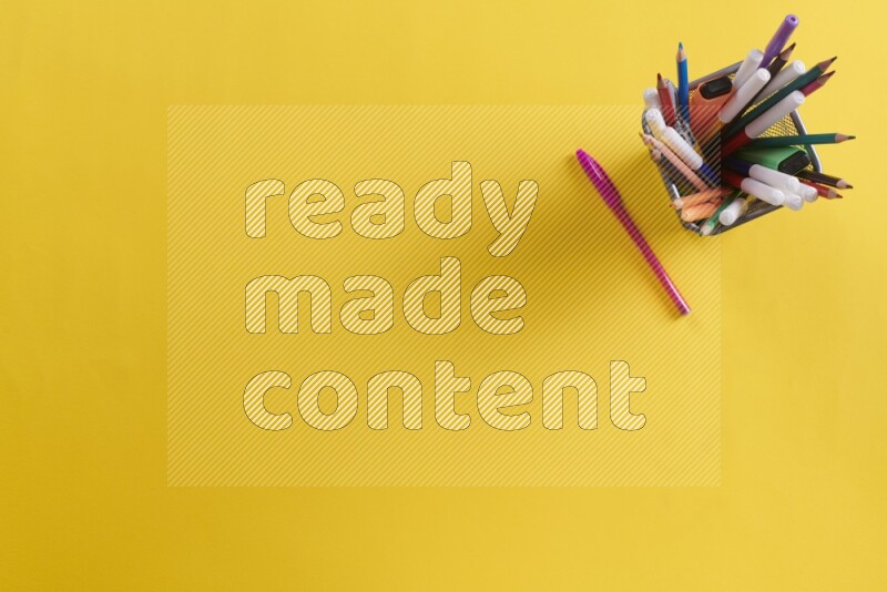 بعض الأقلام والمستلزمات المدرسية في مقلمة معدنية علي خلفية صفراء