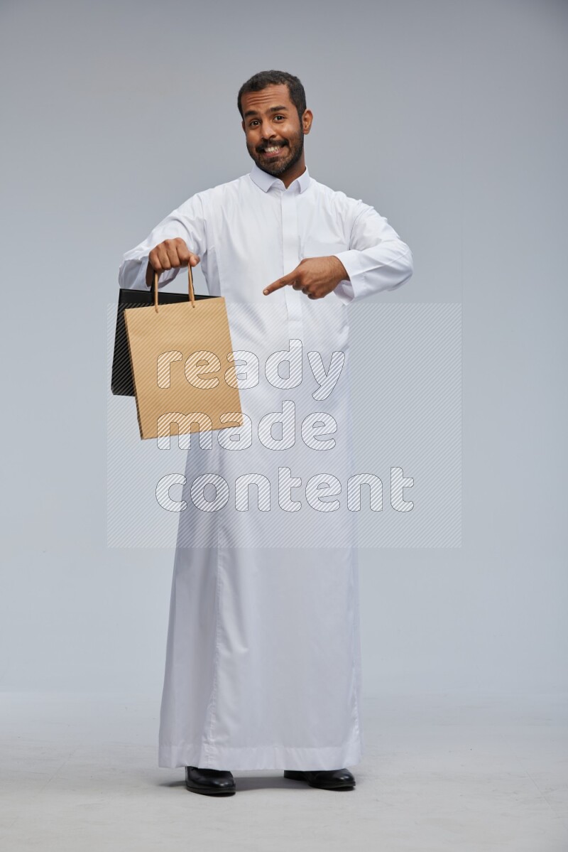 Saudi man Wearing thob standing holding shopping bag on Gray background