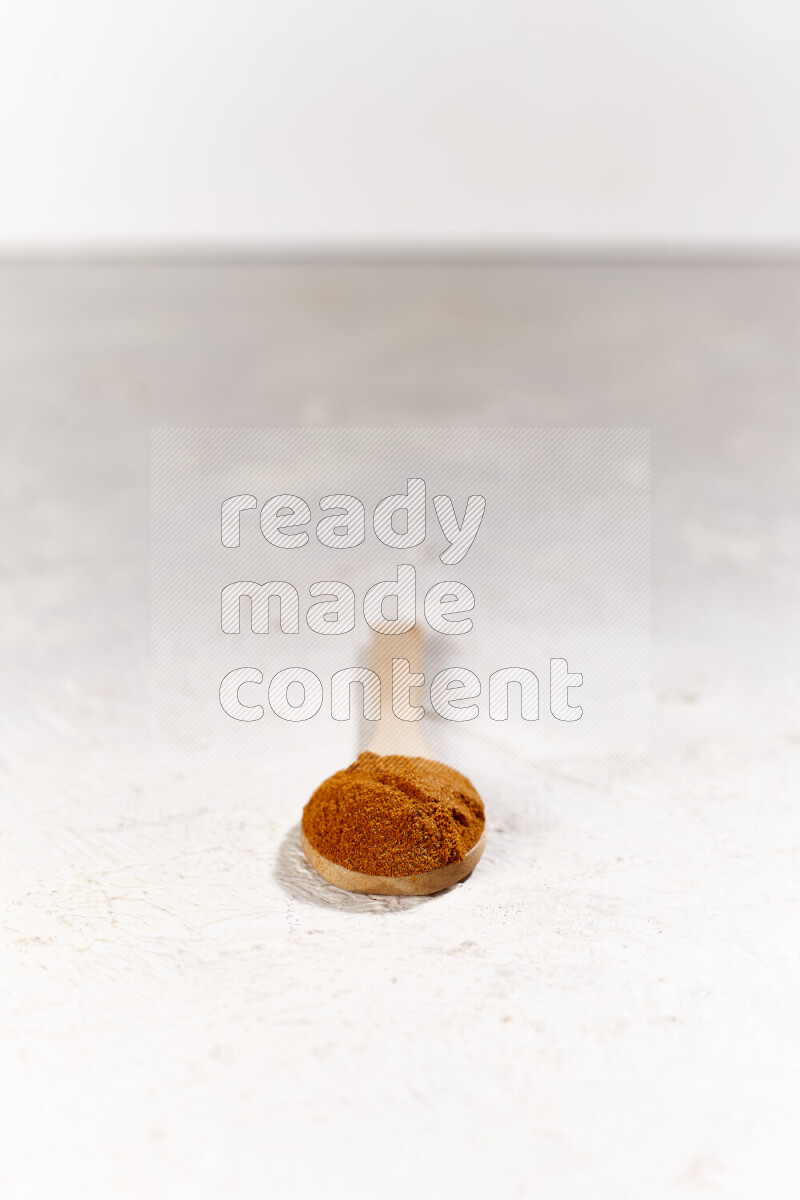 A wooden spoon full of ground paprika powder on white background