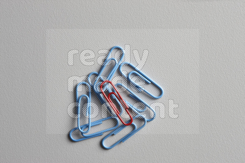 A red paperclip surrounded by bunch of blue paperclips on grey background
