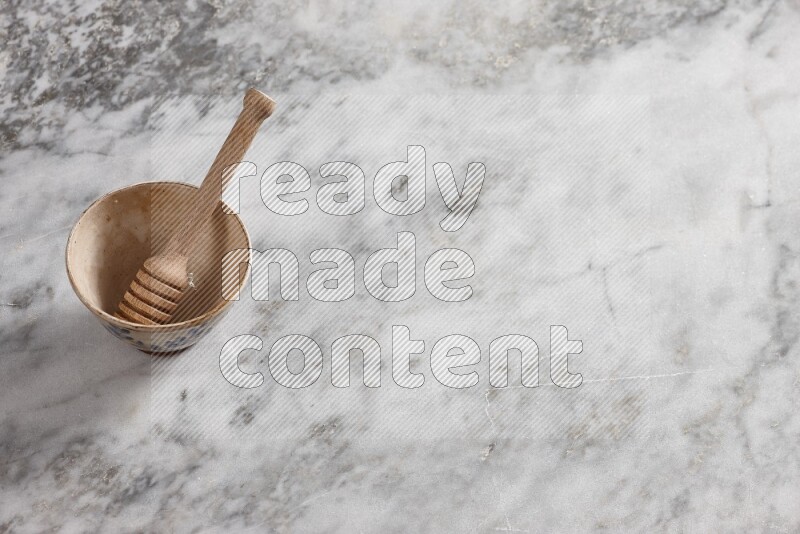 Decorative pottery bowl with wooden honey dipper in it on grey marble background