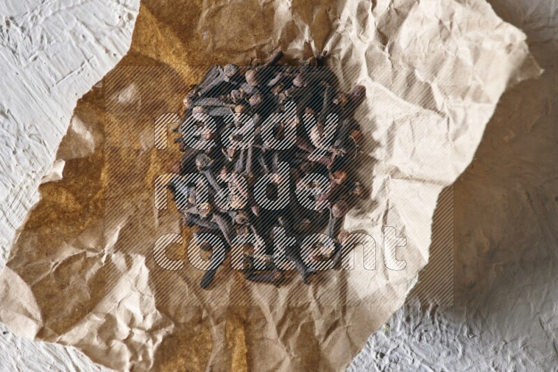 Cloves on crumpled piece of paper on a textured white flooring