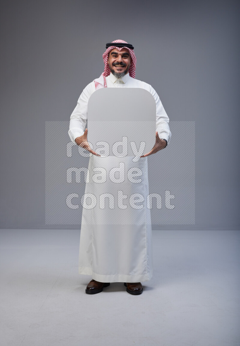 Saudi man Wearing Thob and red Shomag standing holding social media sign on Gray background