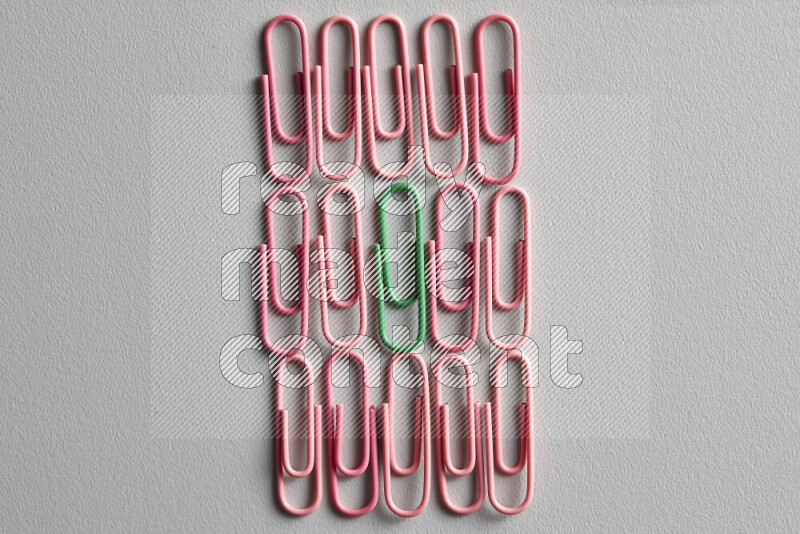A bunch of pink paper clips with a different colored paper clip in the center on grey background