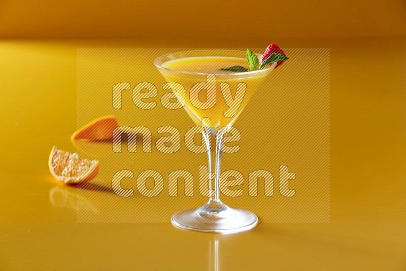 glass of orange juice with berry & mint on yellow background