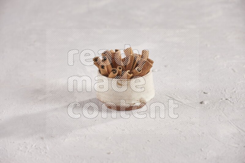 Cinnamon sticks in a beige bowl and more sticks beside it on white background