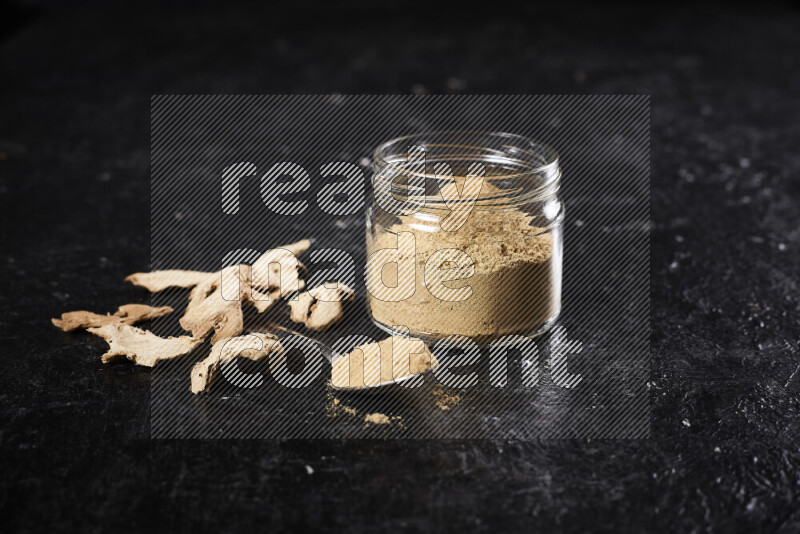 A glass jar full of ground ginger powder on black background