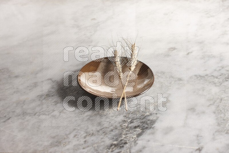Wheat stalks on multicolored pottery plate on grey marble background