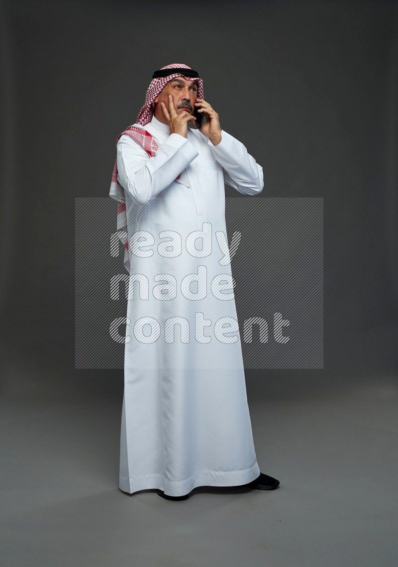 Saudi man with shomag Standing talking on phone on gray background