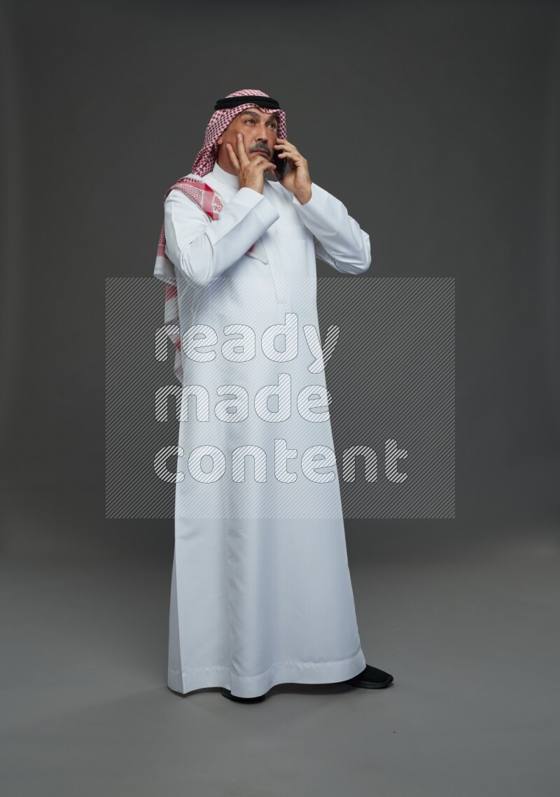 Saudi man with shomag Standing talking on phone on gray background
