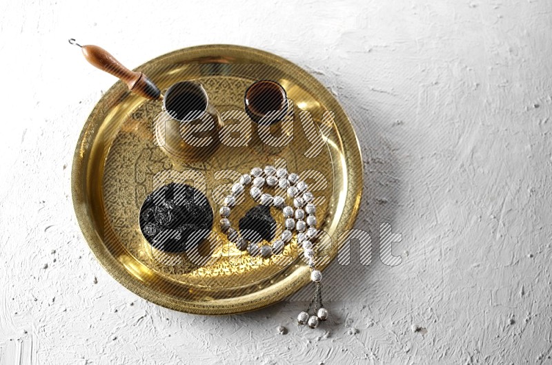 قراصيا في وعاء معدني مع القهوة وسبحة على صينية علي خلفية بيضاء