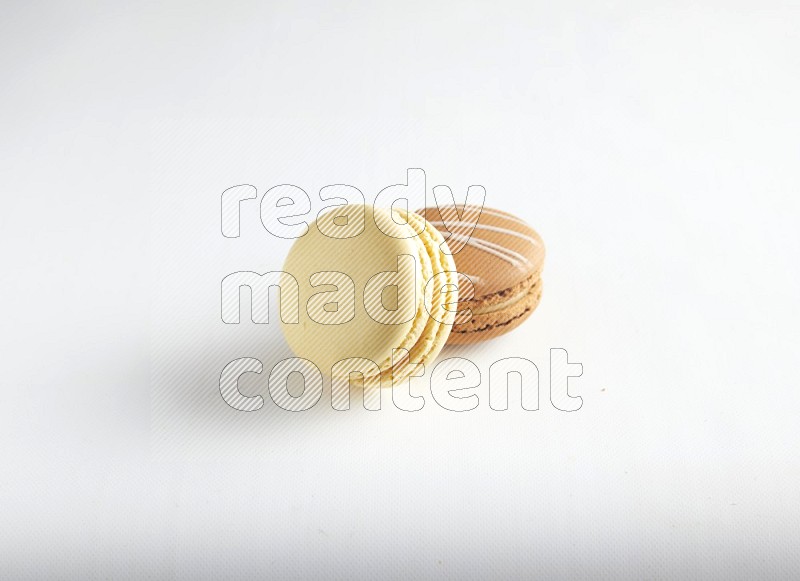 45º Shot of of two assorted Brown Irish Cream, and Yellow Vanilla macarons on white background