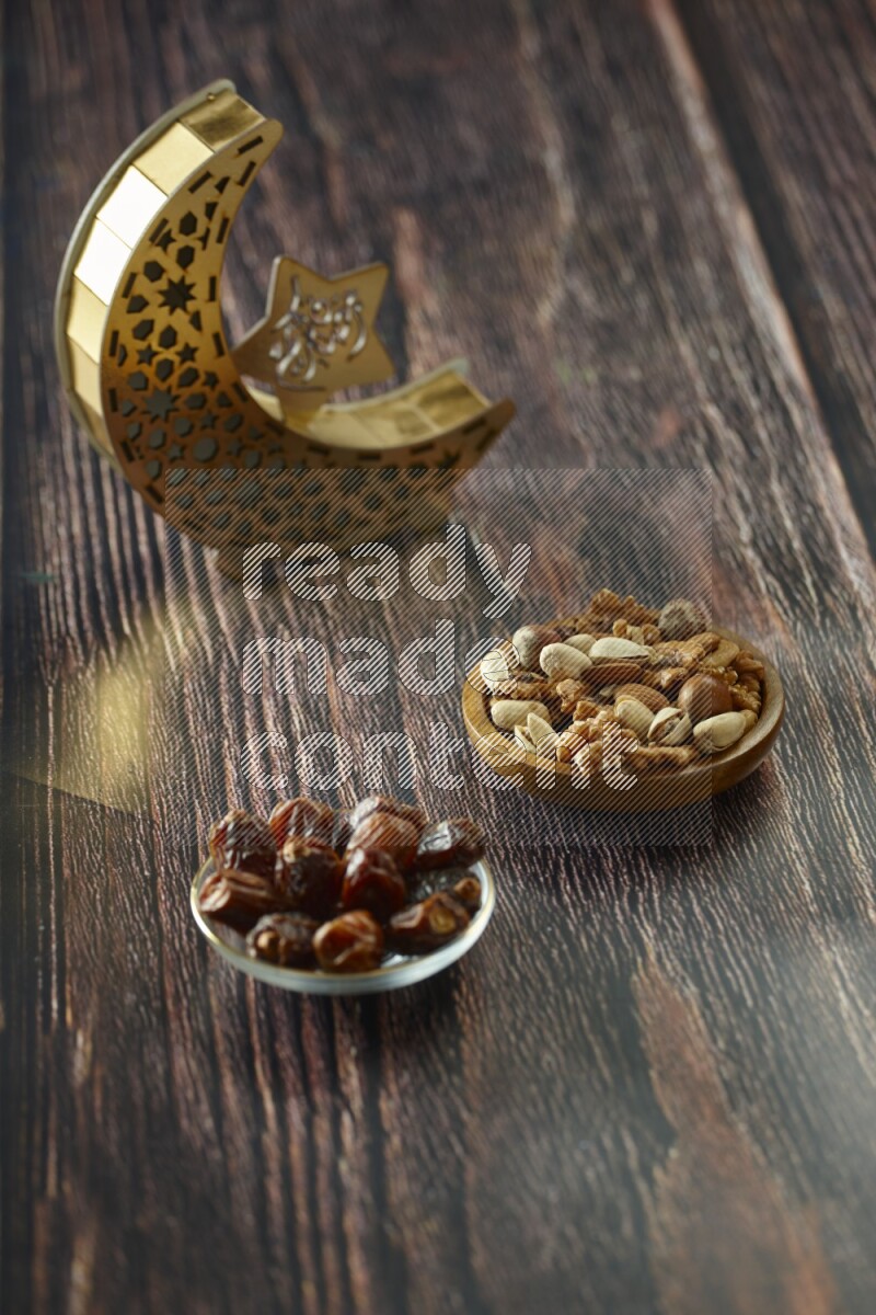 A wooden golden crescent lantern with different drinks, dates, nuts, prayer beads and quran on brown wooden background