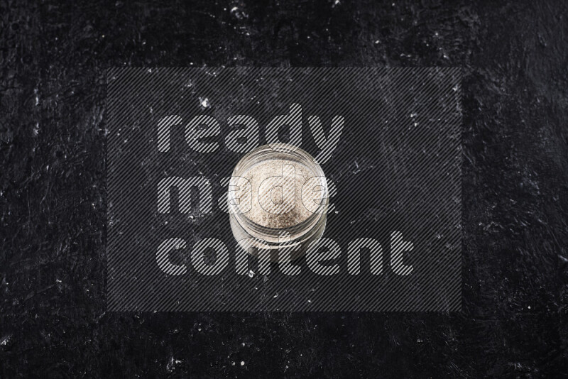 A glass jar full of onion powder on black background