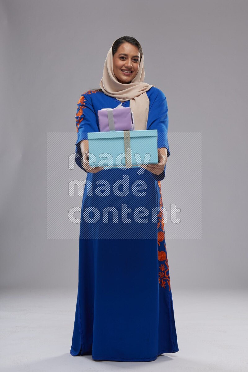 A Saudi woman standing wearing Jalabeya holding a gift box