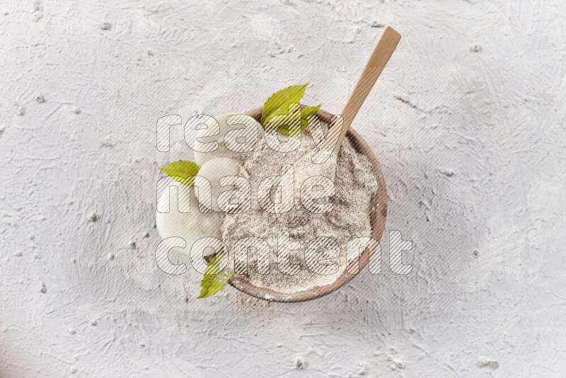 A wooden bowl full of onion powder with a wooden spoon in it with some sliced onions on white background