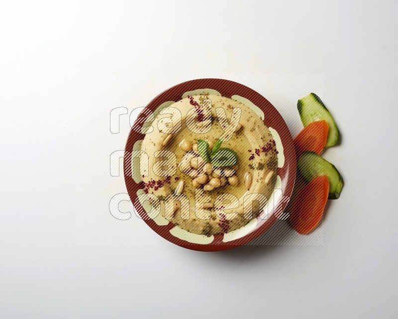 Hummus in a traditional plate garnished with zaatar & sumak on a white background