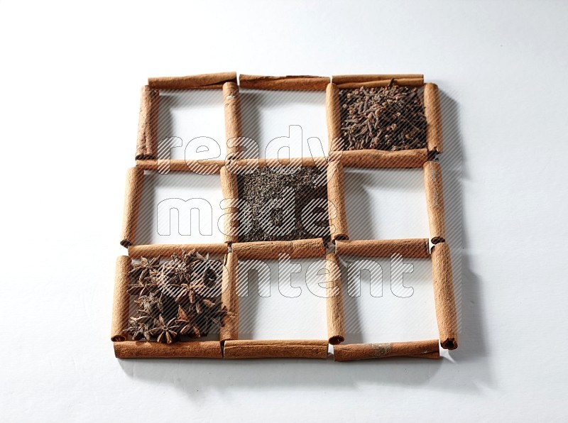 9 squares of cinnamon sticks full of tea in the middle surrounded by nutmeg, dried mint, cloves, dried basil, dried ginger, cinnamon, star anise and cardamom on white flooring