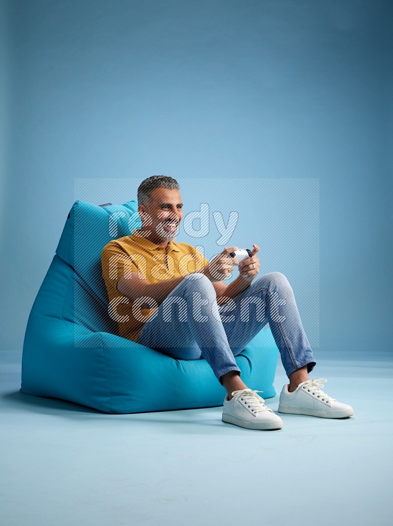 A man sitting on a blue beanbag and gaming with joystick