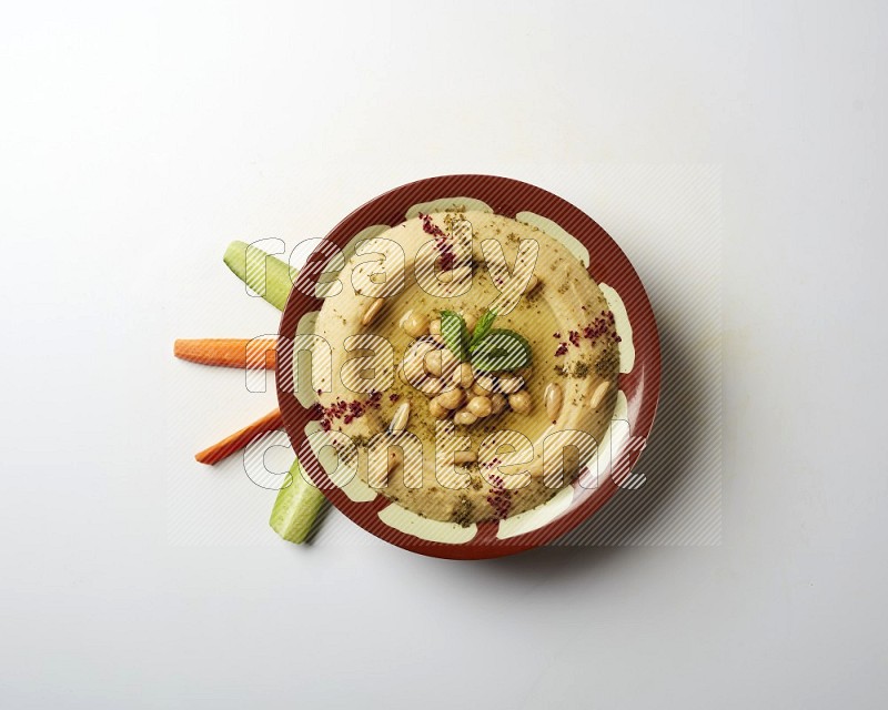 Hummus in a traditional plate garnished with zaatar & sumak on a white background