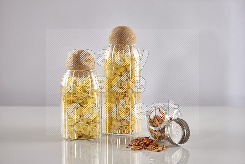 Raw pasta in glass jars with chilis on light grey background