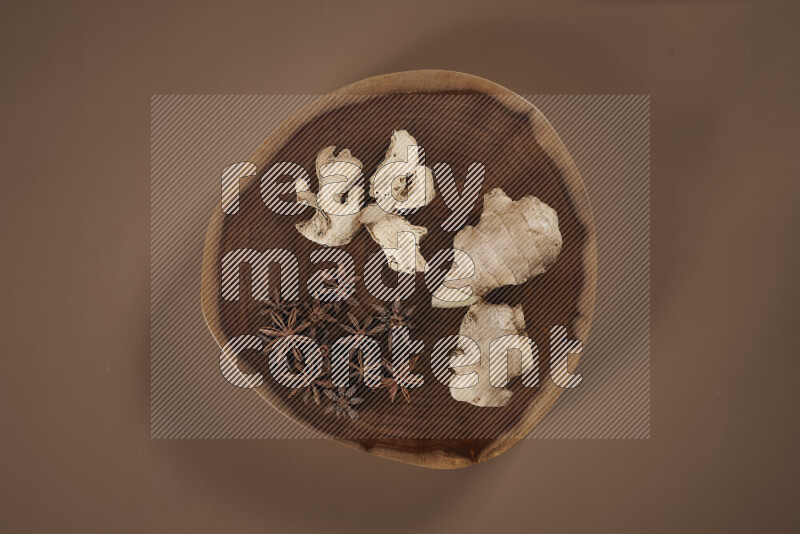 An assorted whole spices on a flat wooden tray including fresh and dried ginger, cinnamon sticks, cardamom, turmeric fingers, cloves, star anise on beige background